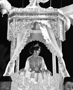 a woman sitting on top of a bed covered in white cloths and gold decorations