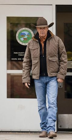 an older man wearing a cowboy hat walks out of a building with his hands in his pockets