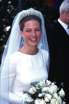 a woman in a wedding dress holding a bouquet and smiling at the camera while standing next to an older man