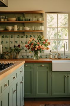 a kitchen filled with lots of green cupboards and flowers in a vase on the counter