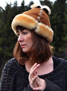 "A playful hat originally designed to accommodate a ponytail emerging from the top of the hat. While this is a fantastic compromise between keeping warm and avoiding hat hair, most fans of this hat don't wear ponytails at all! However, apart from unique styling, we have often heard that fans of this hat like the \"vent\" in the top, citing that it is \"warm, but not claustrophobic.\" This hat is one size, adjustable by tightening or loosening the lacing at the bottom." Brown Sheepskin Hat With Faux Fur Lining, Winter Brown Fur Felt Hat Band, Brown Fur Felt Hat Bands For Winter, High Crown Fur Felt Hat For Winter, Winter High Crown Fur Felt Hat, Brown High Crown Winter Hat, Brown Curved Brim Costume Hat For Winter, Brown Winter Costume Hat With Curved Brim, Lace Ponytail