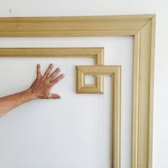 a person's hand reaching for the frame on a white wall with wooden frames