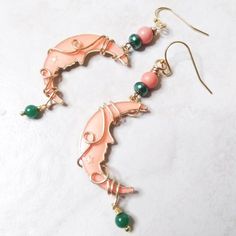 a pair of earrings with pink and green beads on them sitting on a white surface