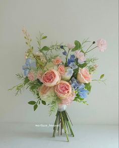 a bouquet of pink, blue and white flowers on a white table top with greenery