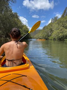 a woman in a yellow kayak paddling down a river with trees on both sides