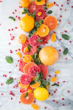 an arrangement of citrus fruits and leaves on a marble surface with pomegranates