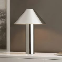 a lamp is sitting on a table next to a white dresser and wall with pictures