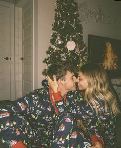 a man and woman in matching pajamas kissing under the christmas tree