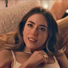 a woman laying on top of a bed wearing a white tank top and gold bracelet