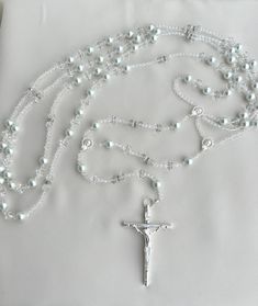 a white beaded rosary with a cross hanging from it's end on a pillow