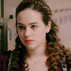 a woman with long curly hair wearing a purple shirt and looking at the camera while standing in front of a door