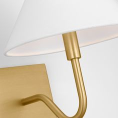 a gold wall light with a white shade on the arm and a metal hook attached to it