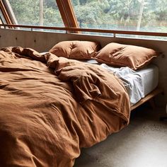 an unmade bed sitting in front of a window with lots of pillows on it