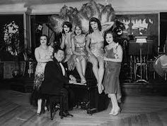 an old black and white photo of women in costumes posing with a man sitting on a piano