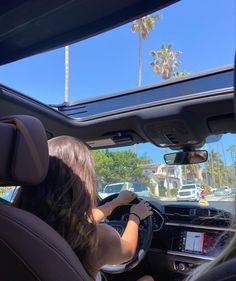 a woman driving a car with palm trees in the background