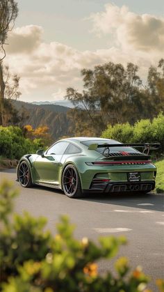 a green sports car parked on the side of a road next to trees and bushes