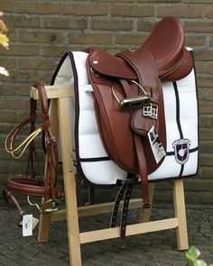 a brown and white horse saddle sitting on top of a wooden stand next to a brick wall