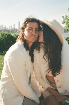 a man and woman sitting next to each other on top of a grass covered field