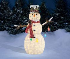 a lighted snowman standing in front of some trees