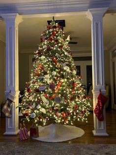 a decorated christmas tree in the corner of a room with white pillars and red and green ornaments