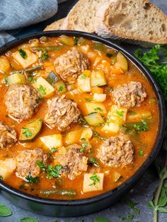 meatball soup in a black bowl with bread and parsley on the side, ready to be eaten