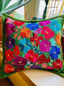 a colorful flowered pillow sitting on top of a wooden bench next to a potted plant