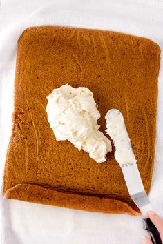 someone is spreading whipped cream on top of a brown piece of cake with a spatula