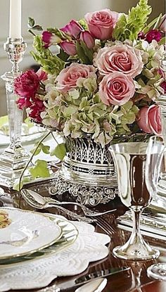 a dining room table is set with silverware and pink roses in a centerpiece