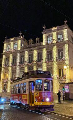 a trolley car driving down the street in front of a building with christmas lights on it