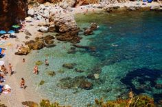 people are on the beach and in the water near some rocks, sand and umbrellas