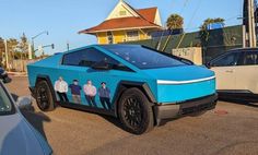 a blue car with people painted on it's side in the street next to parked cars