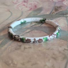 This is a vintage cloisonne bracelet. It is white floral with gold trim. This piece has a hinge and pulls open. There is a chip in the bracelet as you can see in the images as well as specks/pockmarks on the piece. The price reflects this. All sales are final.  The bracelet measures a hair under 2.5 inches across on the interior.  If you have a wish list or are looking for something specific, please ask. I may have exactly what you are looking for. As always please convo me with any questions or concerns regarding this item or with any international shipping questions. Unfortunately I do not accept returns or grant refunds. All shipping fees include handling fees. If you would like to combine shipping costs for more than one item, I would be happy to do so if you convo me before purchase. Antique White Bracelet Jewelry, White Antique Bracelet Jewelry, Collectible White Bracelet Jewelry, White Antique Bracelet, Vintage White Bangle For Wedding, Vintage White Wedding Bangle, Vintage Hand Painted Bracelets As Gift, White Enamel Bangle Jewelry, Hallmarked Vintage White Gold Bangle