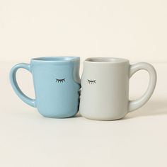 two coffee mugs with eyelashes on them sitting side by side in front of each other