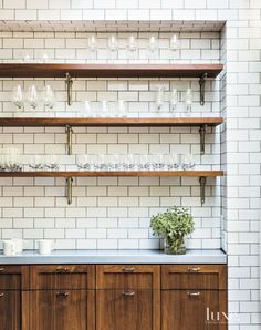 a kitchen with wooden cabinets and shelves filled with glasses on top of each shelf next to a potted plant