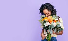 a woman holding a bouquet of flowers in front of her face while standing against a purple wall