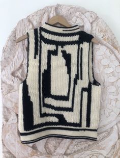 a white and black knitted sweater hanging on a wooden hanger next to a wall