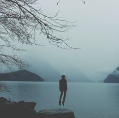 a person standing on the edge of a body of water with mountains in the background