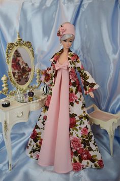 a doll is standing in front of a dressing table with a flowered dress on it