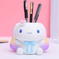 a little white bunny with some pens in it's lap and pen holder on the desk