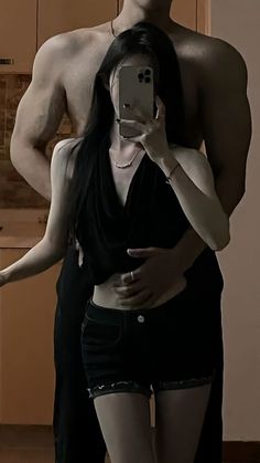 a shirtless man and woman taking a selfie in front of a kitchen mirror