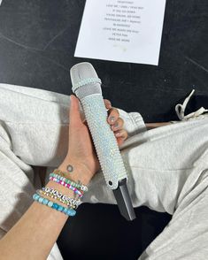 a person holding a microphone with bracelets on their wrist and wearing a white t - shirt