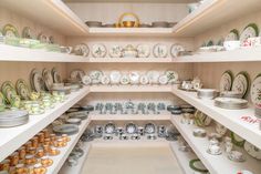 a room filled with lots of plates and bowls on white shelves next to each other