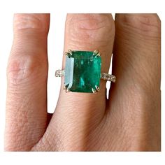 a woman's hand holding an emerald and diamond ring