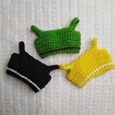 three crocheted items are laying on a white towel and one has a yellow hat