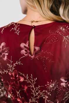 the back of a woman's red dress with flowers on it and a gold chain