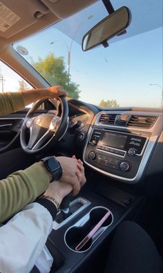 a woman driving a car with her hand on the steering wheel while holding onto an electronic device