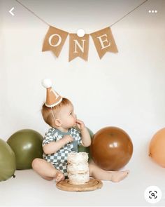 a baby sitting on the floor with a cake in front of him and balloons around him