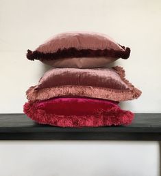 three pillows stacked on top of each other in front of a white wall and black shelf