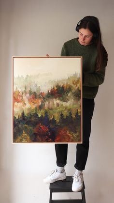 a woman standing on a step stool holding a painting in front of her face and hands