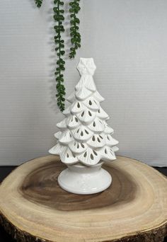 a white ceramic christmas tree sitting on top of a wooden stump